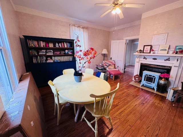 dining room with hardwood / wood-style floors, ceiling fan, a wood stove, and ornamental molding