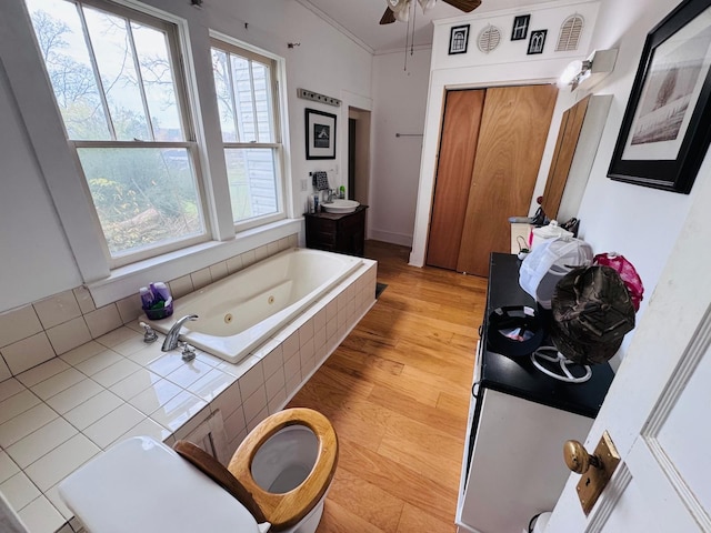 bathroom with ceiling fan, tiled tub, crown molding, hardwood / wood-style floors, and vanity