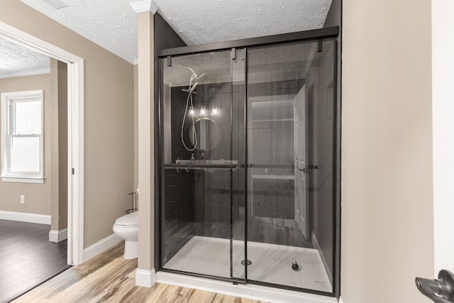 bathroom featuring crown molding, wood-type flooring, a textured ceiling, toilet, and a shower with shower door