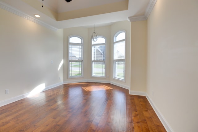 unfurnished room featuring a tray ceiling, dark wood-type flooring, ceiling fan with notable chandelier, and ornamental molding