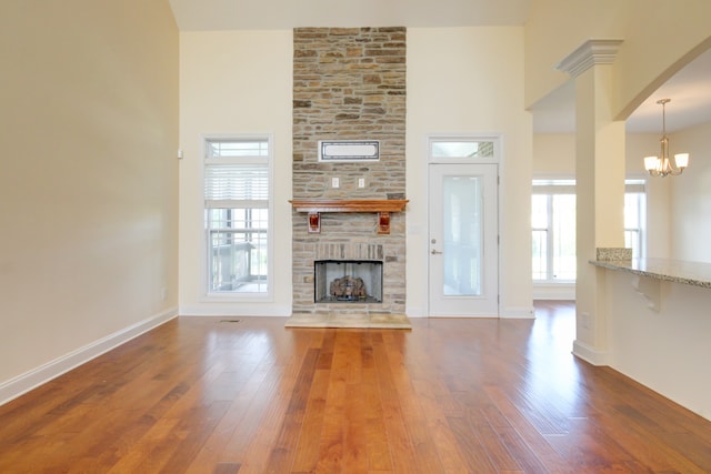 unfurnished living room with a fireplace, wood-type flooring, a notable chandelier, and a high ceiling