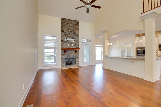 unfurnished living room featuring hardwood / wood-style floors, ceiling fan, a towering ceiling, a fireplace, and decorative columns