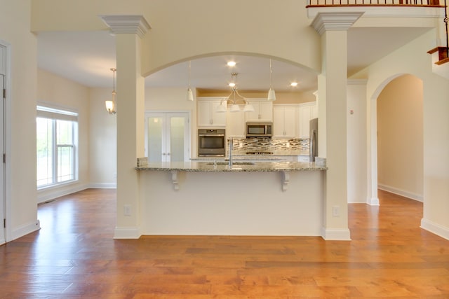 kitchen with appliances with stainless steel finishes, light hardwood / wood-style floors, white cabinetry, and decorative light fixtures