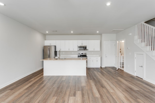 kitchen featuring white cabinets, appliances with stainless steel finishes, a kitchen island with sink, and hardwood / wood-style floors