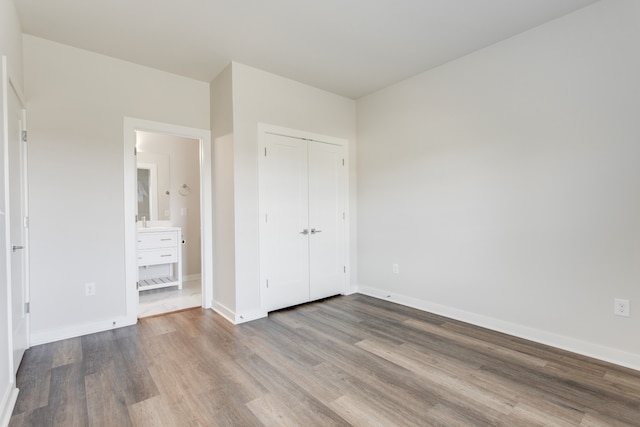 unfurnished bedroom featuring connected bathroom, hardwood / wood-style flooring, and a closet