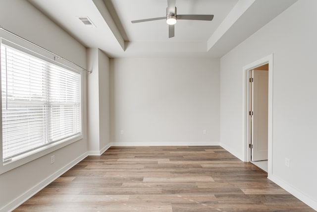 spare room with a raised ceiling, ceiling fan, and light hardwood / wood-style flooring