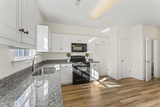 kitchen with sink, dark stone counters, white cabinets, black appliances, and hardwood / wood-style flooring