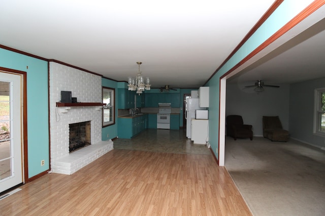 unfurnished living room featuring a brick fireplace, ceiling fan with notable chandelier, crown molding, sink, and light hardwood / wood-style floors