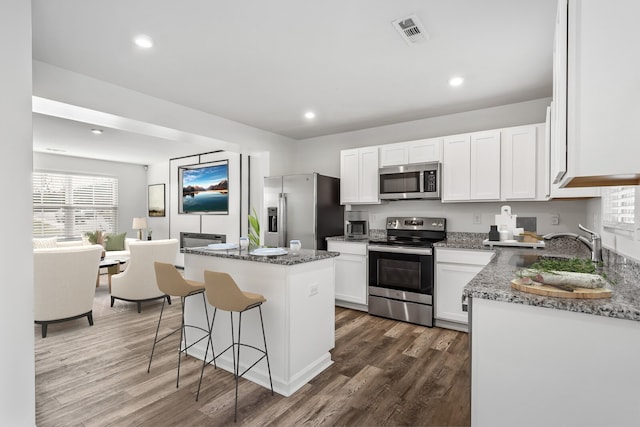 kitchen featuring white cabinetry, a center island, stainless steel appliances, light stone counters, and dark hardwood / wood-style flooring