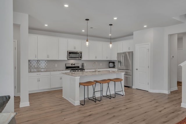 kitchen featuring white cabinets, light wood-type flooring, stainless steel appliances, and a center island with sink