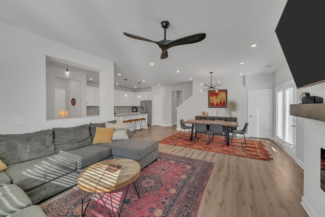 living room featuring ceiling fan with notable chandelier and light hardwood / wood-style floors