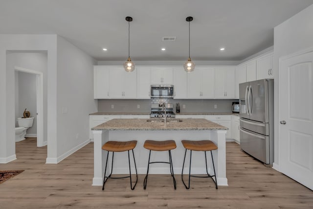 kitchen with a kitchen island with sink, light hardwood / wood-style flooring, appliances with stainless steel finishes, light stone counters, and white cabinetry