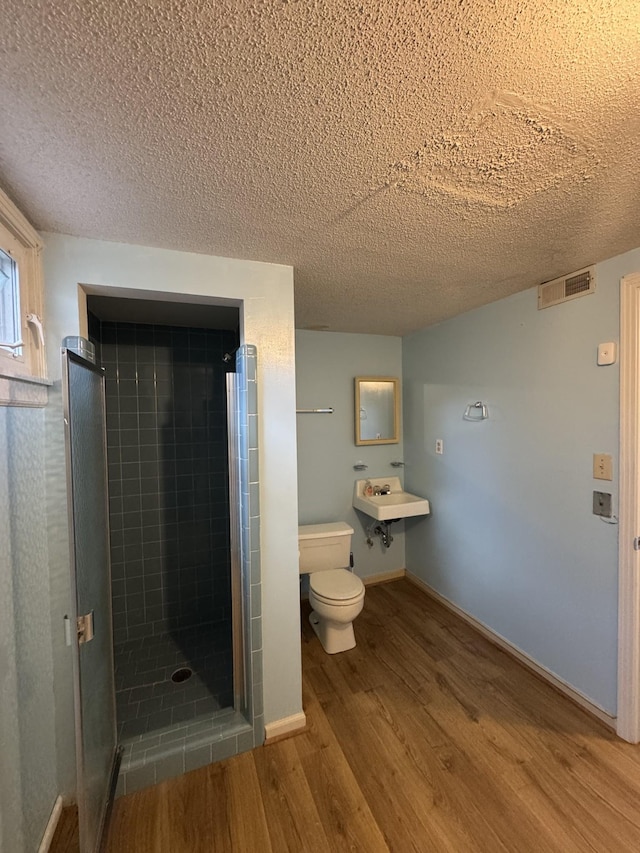 bathroom with a tile shower, a textured ceiling, hardwood / wood-style flooring, and toilet