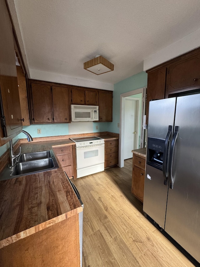 kitchen featuring dark brown cabinets, a textured ceiling, white appliances, sink, and light hardwood / wood-style flooring