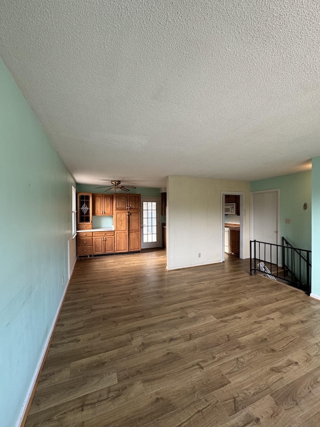 unfurnished living room featuring dark hardwood / wood-style floors, ceiling fan, and a textured ceiling