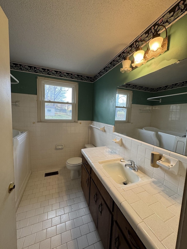 bathroom featuring vanity, tile patterned flooring, independent washer and dryer, a textured ceiling, and tile walls