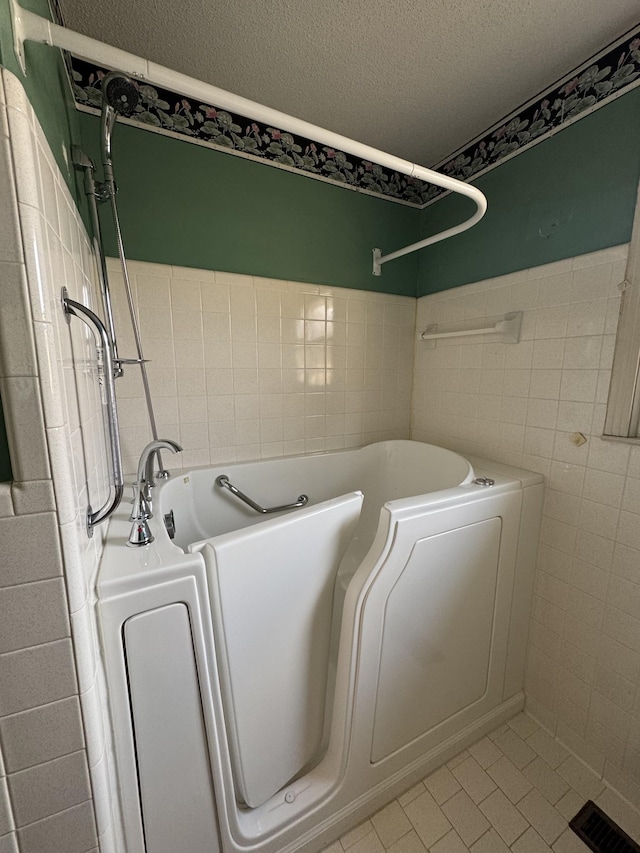 bathroom with tile patterned flooring, washer / clothes dryer, a textured ceiling, a bathtub, and tile walls