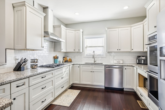 kitchen with sink, stainless steel appliances, wall chimney range hood, dark hardwood / wood-style floors, and decorative backsplash