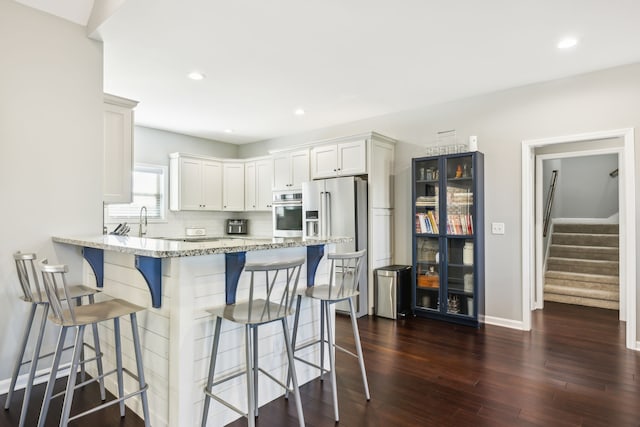 kitchen with a kitchen bar, dark hardwood / wood-style flooring, light stone counters, stainless steel appliances, and white cabinetry