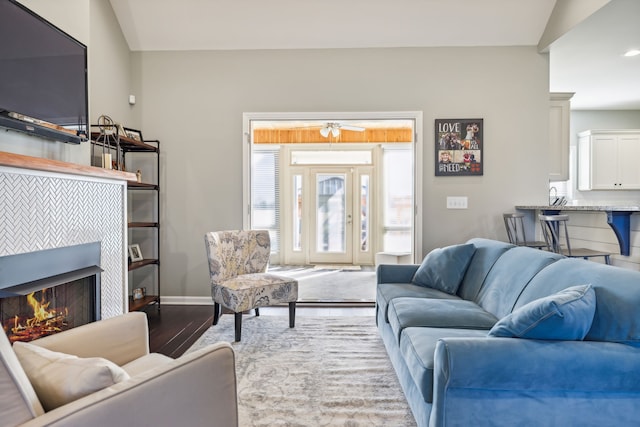 living room featuring a tiled fireplace, ceiling fan, hardwood / wood-style floors, and vaulted ceiling