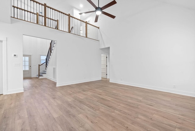 unfurnished living room with a high ceiling, ceiling fan, and light wood-type flooring