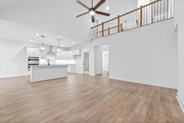 unfurnished living room with ceiling fan, sink, a high ceiling, and light wood-type flooring