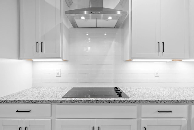 kitchen with light stone counters, wall chimney range hood, backsplash, black electric stovetop, and white cabinets