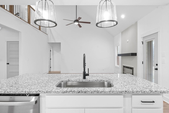 kitchen with light stone counters, sink, hanging light fixtures, and white cabinets