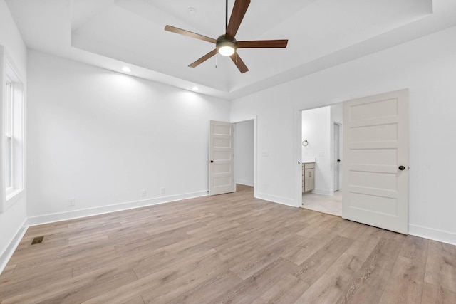 unfurnished bedroom featuring a tray ceiling, light hardwood / wood-style flooring, ceiling fan, and ensuite bathroom