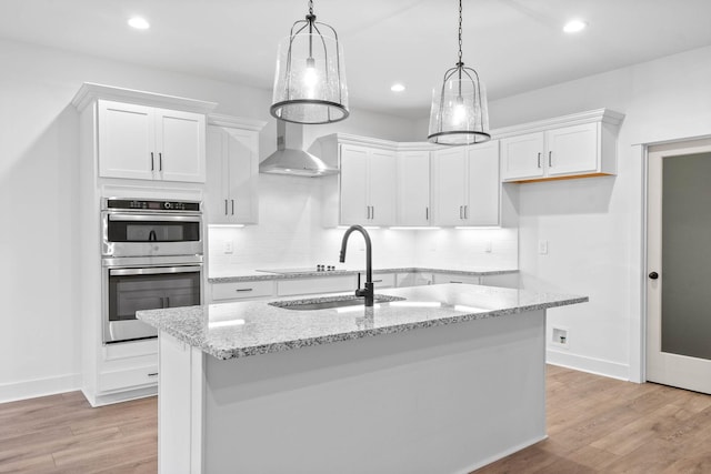 kitchen featuring white cabinetry, hanging light fixtures, light stone countertops, a center island with sink, and stainless steel double oven