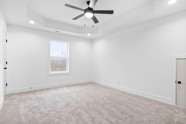 empty room featuring light colored carpet, a raised ceiling, and ceiling fan