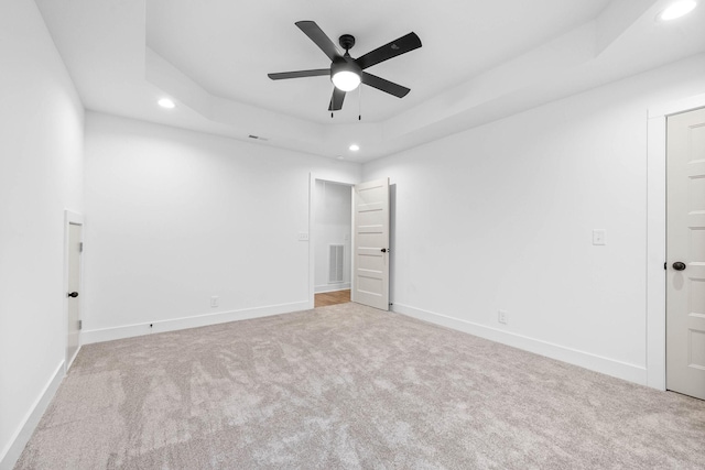 spare room featuring ceiling fan, a tray ceiling, and light carpet