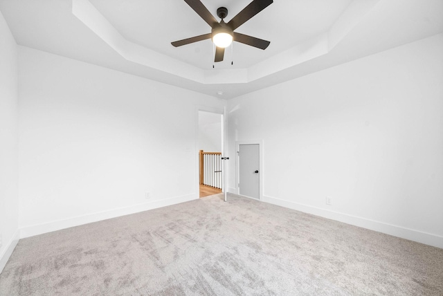 unfurnished room featuring ceiling fan, light colored carpet, and a raised ceiling