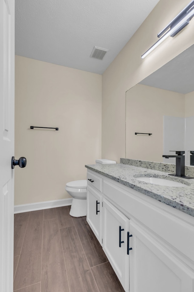 bathroom featuring hardwood / wood-style floors, vanity, toilet, and a textured ceiling