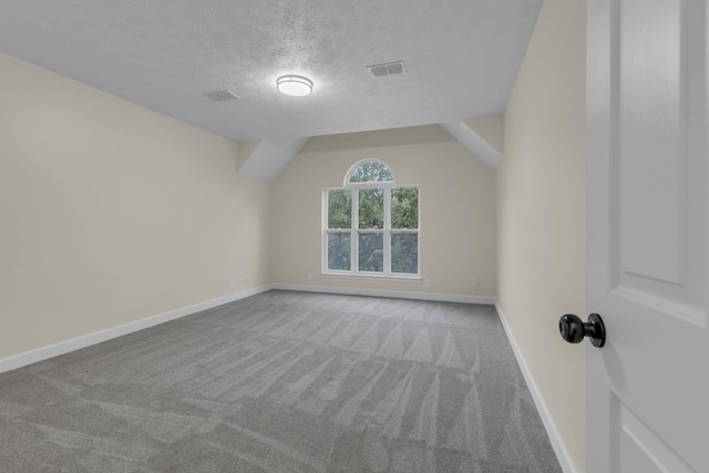 unfurnished room with light colored carpet, a textured ceiling, and vaulted ceiling