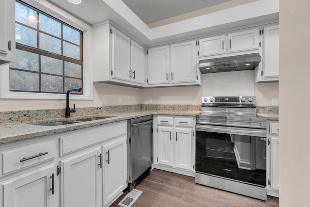 kitchen with light stone countertops, white cabinetry, sink, stainless steel appliances, and hardwood / wood-style flooring