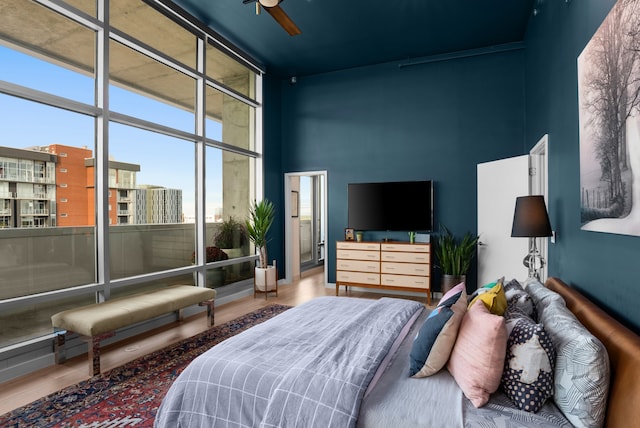 bedroom with ceiling fan, floor to ceiling windows, wood-type flooring, and a towering ceiling