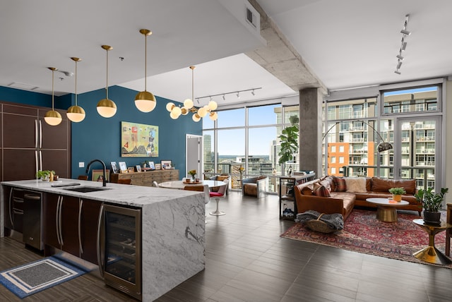 kitchen featuring sink, rail lighting, wine cooler, light stone counters, and decorative light fixtures