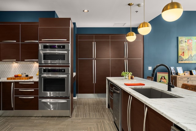 kitchen featuring light stone countertops, appliances with stainless steel finishes, tasteful backsplash, sink, and decorative light fixtures