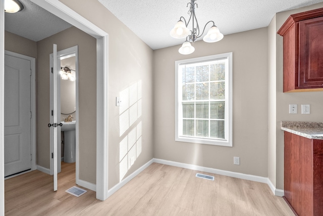 unfurnished dining area with a notable chandelier, light wood-type flooring, and a textured ceiling