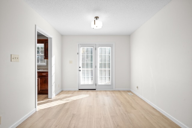 doorway to outside with light hardwood / wood-style floors, a textured ceiling, and a wealth of natural light