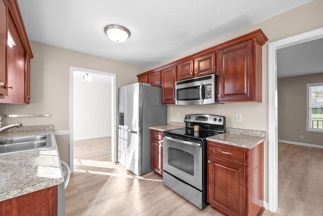 kitchen featuring sink, light hardwood / wood-style flooring, a textured ceiling, appliances with stainless steel finishes, and light stone counters