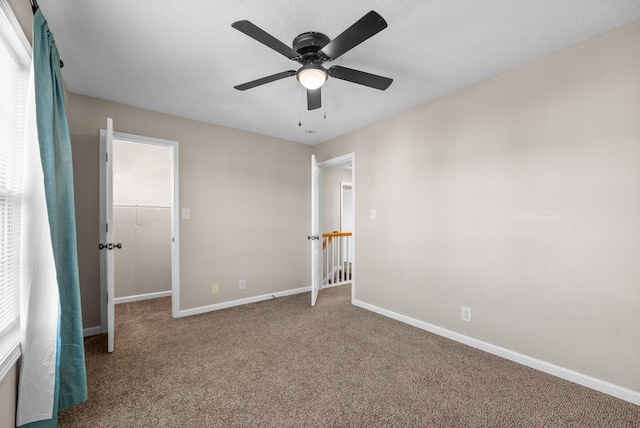 unfurnished bedroom featuring carpet flooring, ceiling fan, and a spacious closet