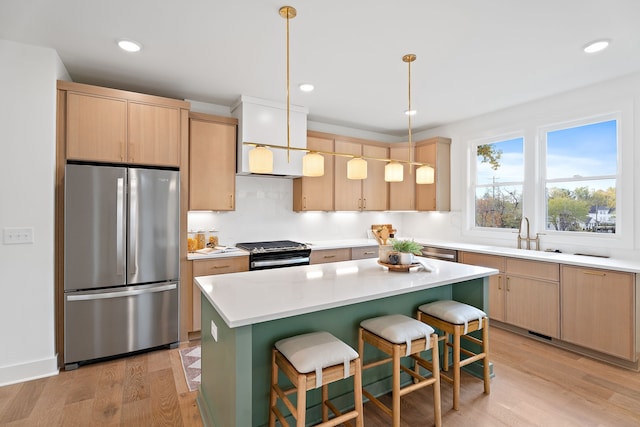 kitchen with hanging light fixtures, sink, light wood-type flooring, appliances with stainless steel finishes, and a kitchen island