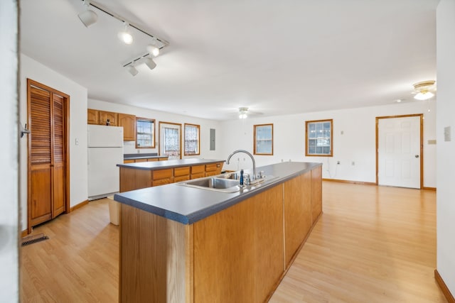 kitchen featuring sink, white refrigerator, plenty of natural light, a center island with sink, and light wood-type flooring