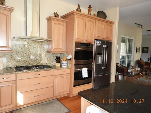 kitchen featuring wall chimney exhaust hood, light brown cabinetry, light hardwood / wood-style floors, light stone counters, and stainless steel appliances