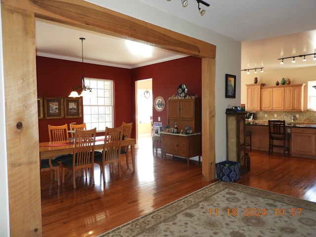 dining area featuring an inviting chandelier, rail lighting, dark wood-type flooring, and ornamental molding