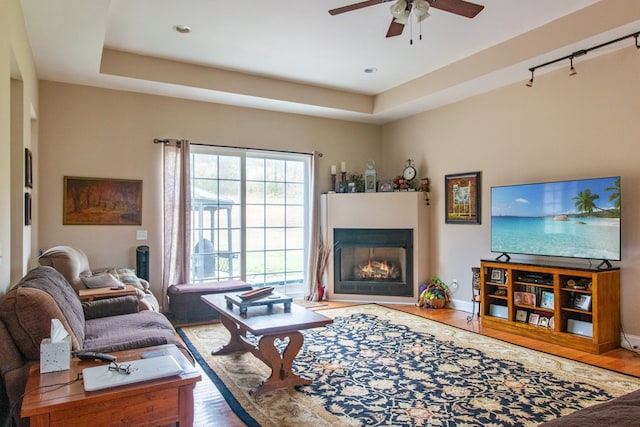 living room featuring hardwood / wood-style floors, ceiling fan, and a raised ceiling