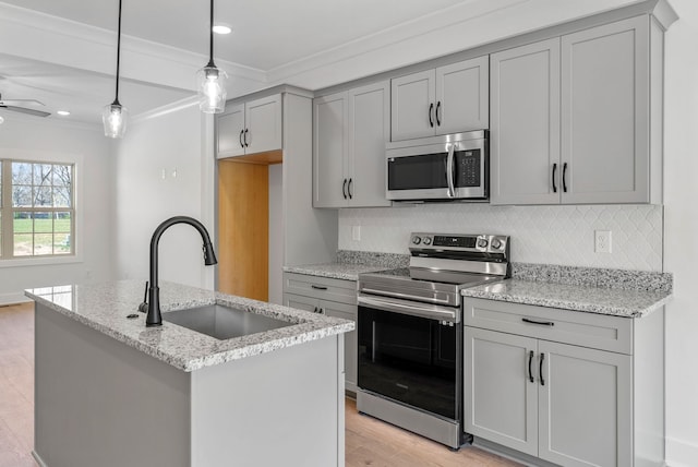 kitchen featuring light stone counters, stainless steel appliances, sink, pendant lighting, and light hardwood / wood-style flooring