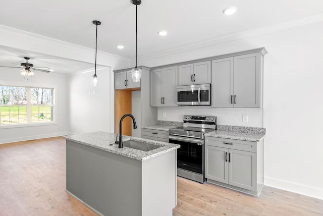 kitchen featuring light stone countertops, ceiling fan, sink, stainless steel appliances, and a kitchen island with sink